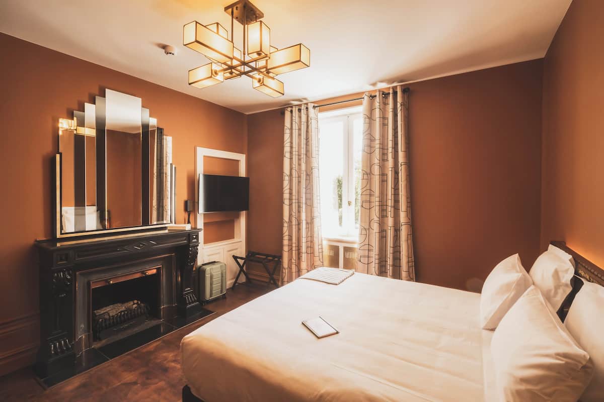 Habitación de hotel con una cama grande, una chimenea, un televisor de pantalla plana y un ventanal con cortinas.
