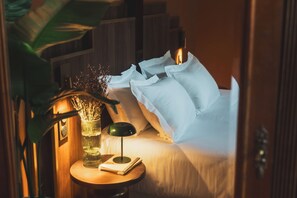 A neatly made bed with white linens and pillows, a bedside table with a lamp and a book, and a vase with dried flowers. - Parc Victoria Hôtel (Saint-Jean-de-Luz)