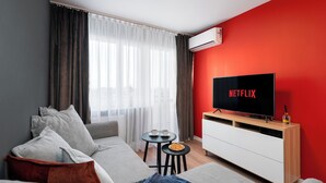 A modern living room with a sofa, a small table with cups, a TV displaying 'NETFLIX', and a red accent wall.