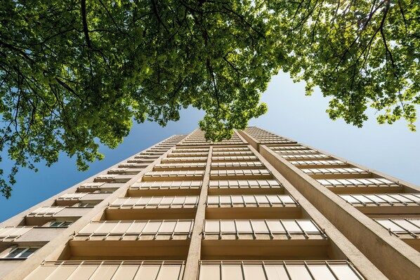 Un edificio alto con varios pisos, grandes ventanales y vistas al cielo entre el follaje.