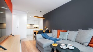 A modern living room with a grey sofa, a wooden coffee table, and a dining area with a table and chairs.