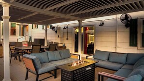 An outdoor patio with a covered seating area, a fire feature, and a fan. - Cosmopolitan- Hot Tub, Heated Pool & Fire Pit (Fredericksburg)