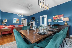 A dining room with a wooden table set for six, teal chairs, and a chandelier. - Cosmopolitan- Hot Tub, Heated Pool & Fire Pit (Fredericksburg)