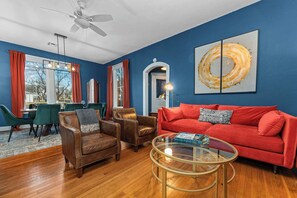 A living room with a red sofa, leather chairs, a glass coffee table, and a dining area with green chairs. - Cosmopolitan- Hot Tub, Heated Pool & Fire Pit (Fredericksburg)