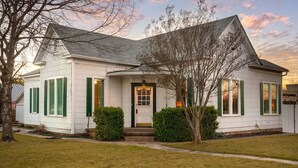 A white house with green shutters, a front door, and a small front yard. - Cosmopolitan- Hot Tub, Heated Pool & Fire Pit (Fredericksburg)