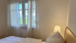 Un dormitorio con cama, ventana con cortinas y una lámpara de noche.