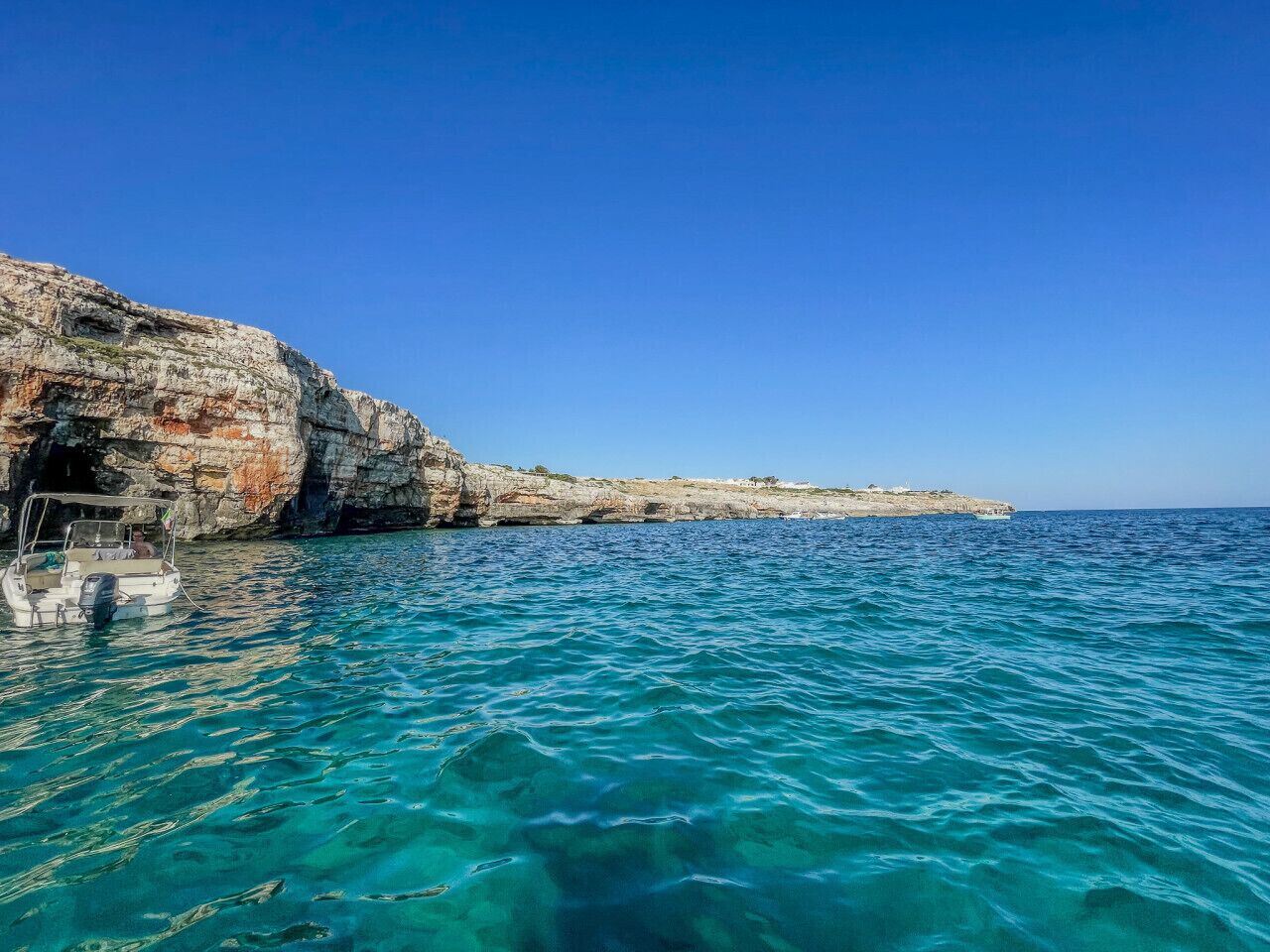 A boat anchored near a rocky coastline with clear blue water.