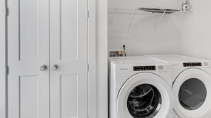 Two front-loading washing machines sit on a countertop, accompanied by a simple wardrobe with two doors.