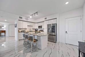 Una cocina moderna con armarios blancos, un refrigerador de acero inoxidable y piso de mármol.