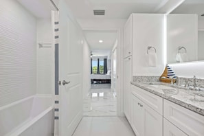 A modern bathroom with a bathtub, a large mirror, and a marble countertop. - Waterfront condo w/ pool, hot tub & sauna (Merritt Island)