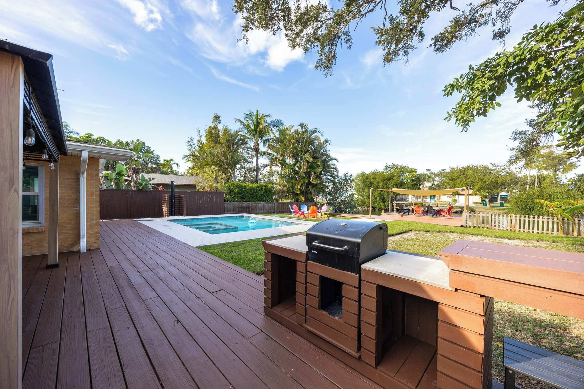 Outdoor deck with built-in grill overlooking a pool and shaded seating area in a tropical backyard