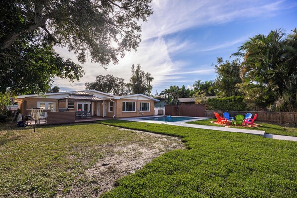 A two-story house with a swimming pool, a patio with outdoor furniture, and a well-maintained lawn.