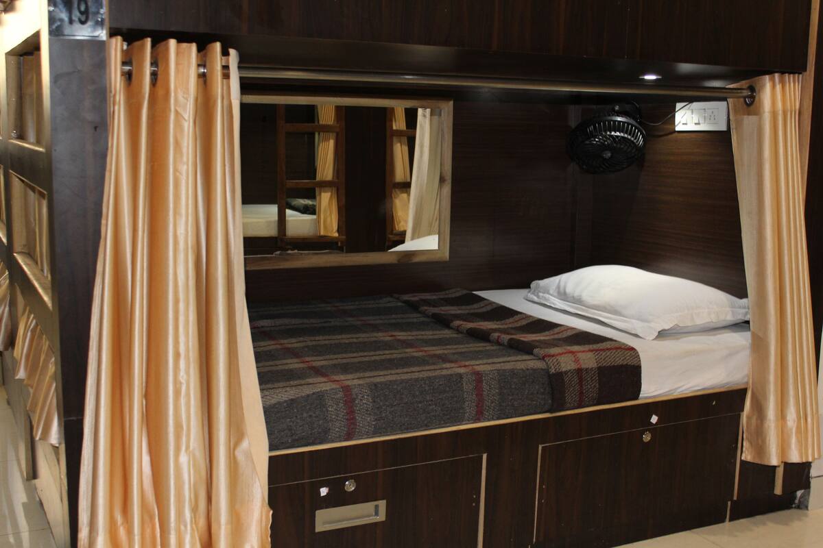 Quarto compacto com uma cama de solteiro, janela com cortinas, mesa de cabeceira pequena e cabeceira.
