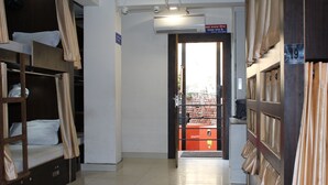 Un couloir d’hôtel avec des lits superposés sur la gauche, une porte donnant sur un mur de briques, et une enseigne Mahindra visible à travers la porte.