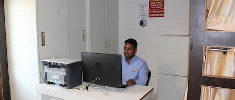 Un homme est assis à un bureau, devant un ordinateur et une imprimante, avec un meuble en arrière-plan.
