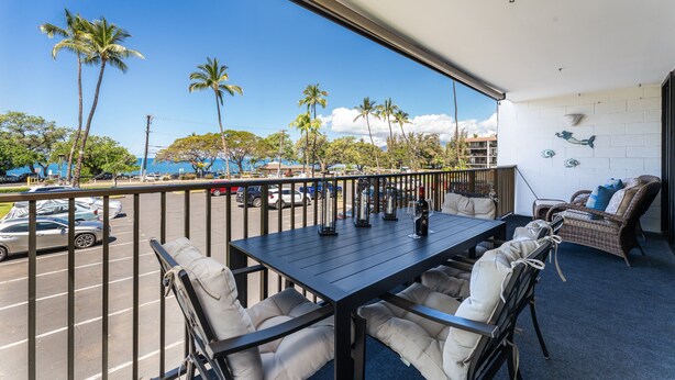 Un balcon avec une table, des chaises et une vue sur la rue et les palmiers.