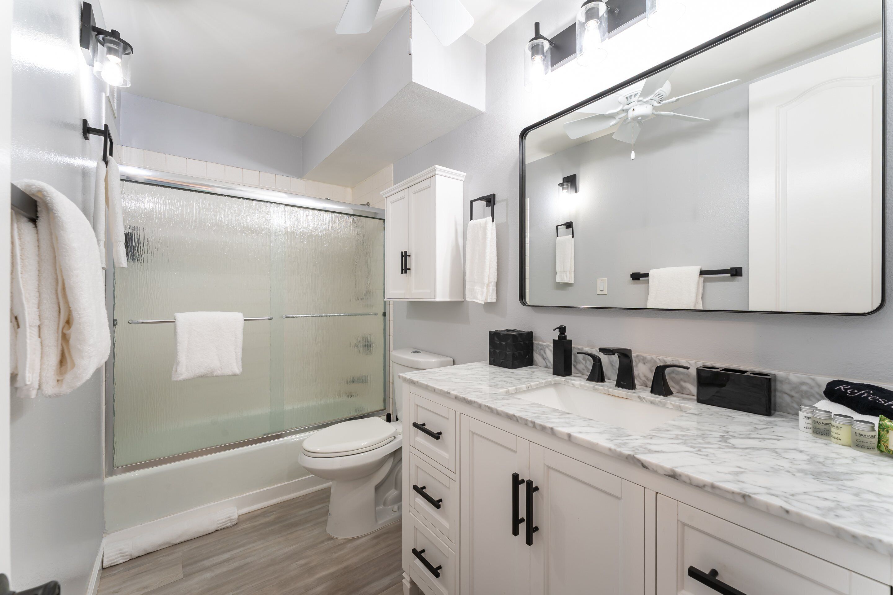 A modern bathroom with a glass-enclosed shower, a toilet, a sink with a marble countertop, and a large mirror.
