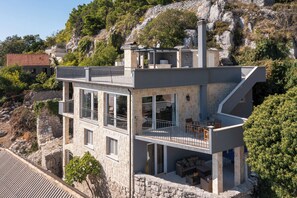 Et moderne hus i to etager med stenvæg, flere balkoner og udsigt til en bakket landskab.