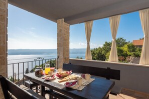 En balkon med et bord dækket til morgenmad, med udsigt over et smukt hav- og bjerglandskab.