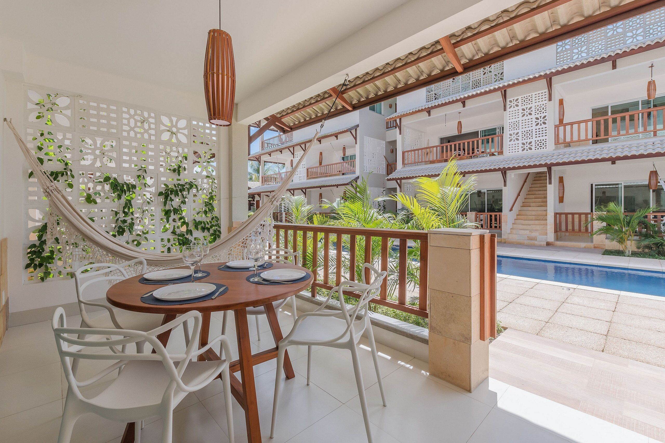 A dining area with a table set for four, surrounded by white chairs, a hammock, and a decorative white lattice wall.