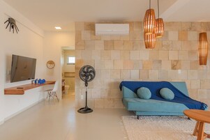 Uma sala de estar moderna com um sofá azul, uma televisão, um ventilador e uma parede de pedra.
