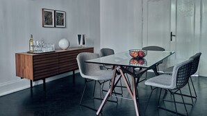 Een moderne eetruimte met een glazen tafel, metalen stoelen, een houten buffetkast en een decoratieve plafondventilator.