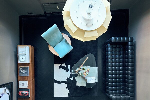 A modern interior with a black leather sofa, a wooden cabinet with framed items, and a wall-mounted clock. - Design Apartments am Römerturm (Cologne)