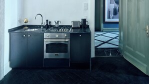 Een moderne keuken met een zwart aanrecht, roestvrijstalen apparatuur en uitzicht op de straat door een geopende deur.