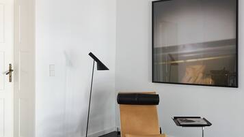 A room with a black hexagonal floor, a white door, a black floor lamp, a massage table, and a framed picture on the wall.