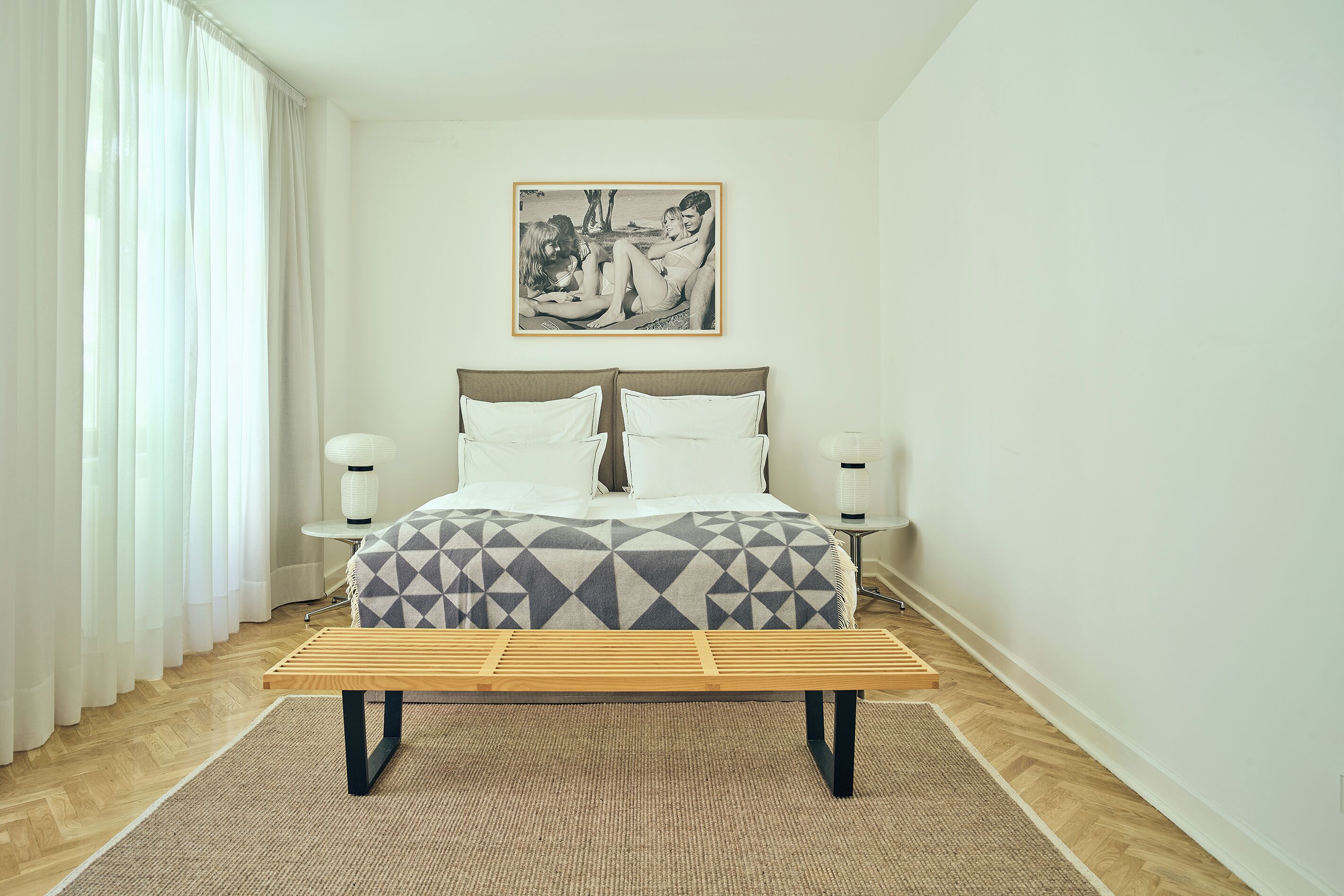 A bedroom with a bed, bedside tables, a bench, and a picture on the wall.