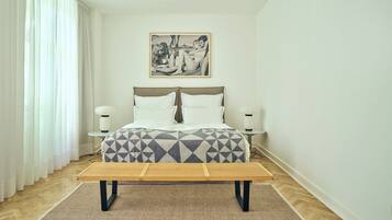 A bedroom with a bed, bedside tables, a bench, and a picture on the wall.