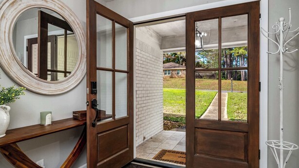 A doorway with a wooden frame, a doormat, and a white wall with a round mirror.
