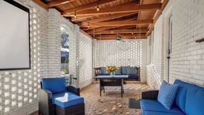 An outdoor patio with a brick wall, a blue sofa, a wicker chair, and a table with flowers.