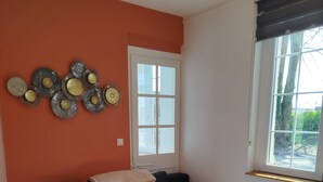 Un salon avec un canapé noir, un tapis à motifs, une table basse, des assiettes décoratives accrochées au mur et une fenêtre avec des stores.