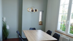 Une pièce avec une table en bois, des chaises noires, un élément décoratif mural, une plante en pot et une fenêtre donnant sur un paysage verdoyant.