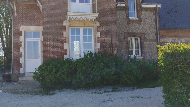 Une maison à deux étages, construite en briques, avec un porche à l’avant, un petit jardin et une allée gravillonnée.