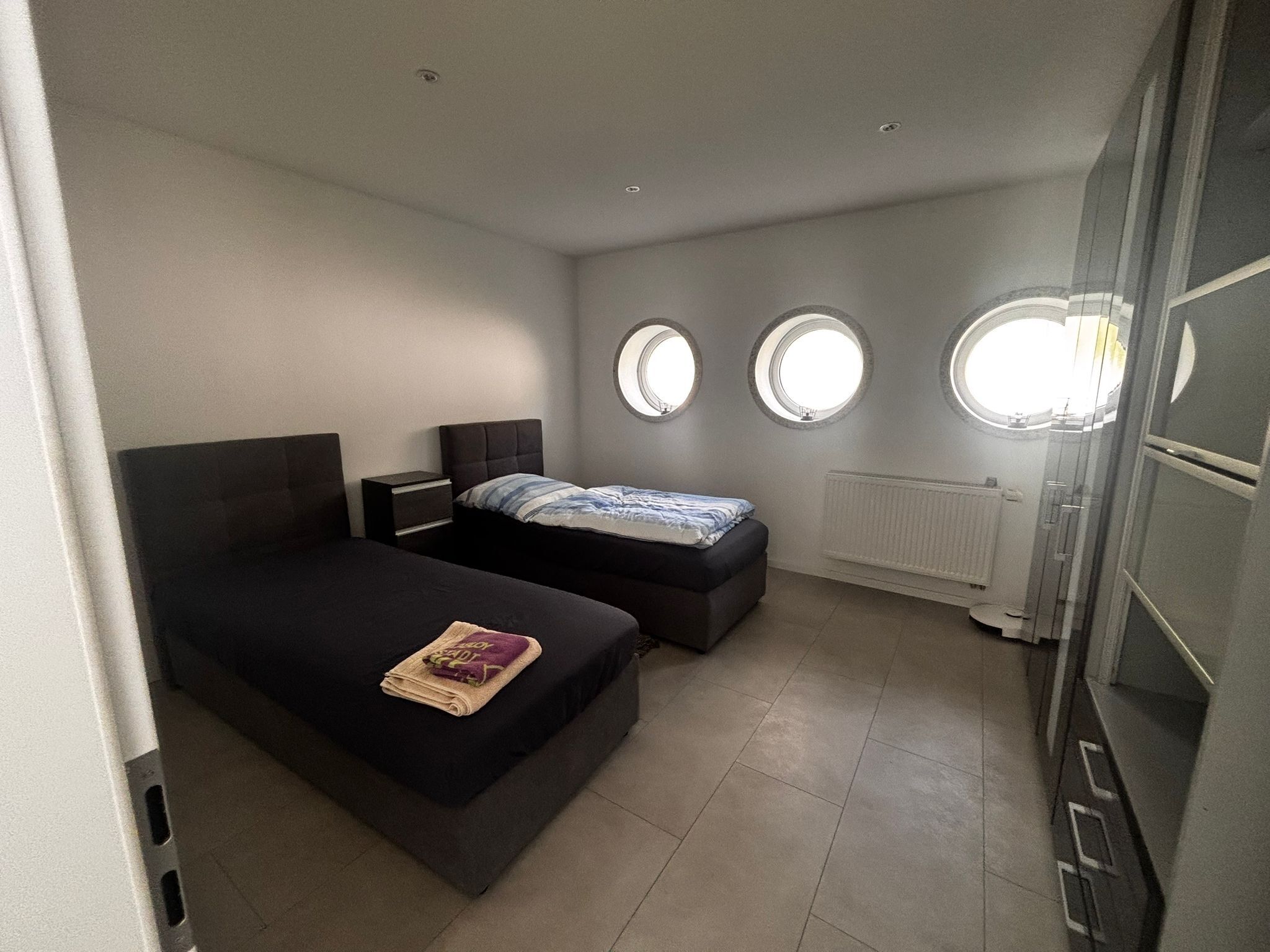 Un dormitorio con dos camas, un radiador y tres ventanas redondas.