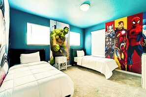 Quarto com duas camas, um grande mural de super-heróis na parede e janela com persianas.