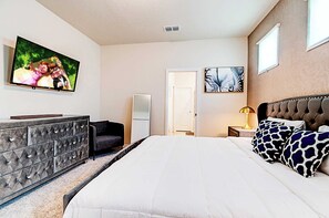 A bedroom with a bed, a dresser, a chair, a TV, and artwork on the walls. - Game Room & Private Pool! Windsor Cay 5BR Home (Clermont)