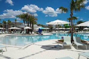 A pool area with lounge chairs and umbrellas, surrounded by palm trees and a clear blue sky. - Game Room & Private Pool! Windsor Cay 5BR Home (Clermont)