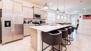 A modern kitchen with a central island, stainless steel appliances, pendant lighting, and bar stools. - Game Room & Private Pool! Windsor Cay 5BR Home (Clermont)