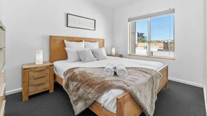 Une chambre à coucher avec un lit en bois, une literie grise, un plaid en fourrure et une fenêtre donnant sur la ville.