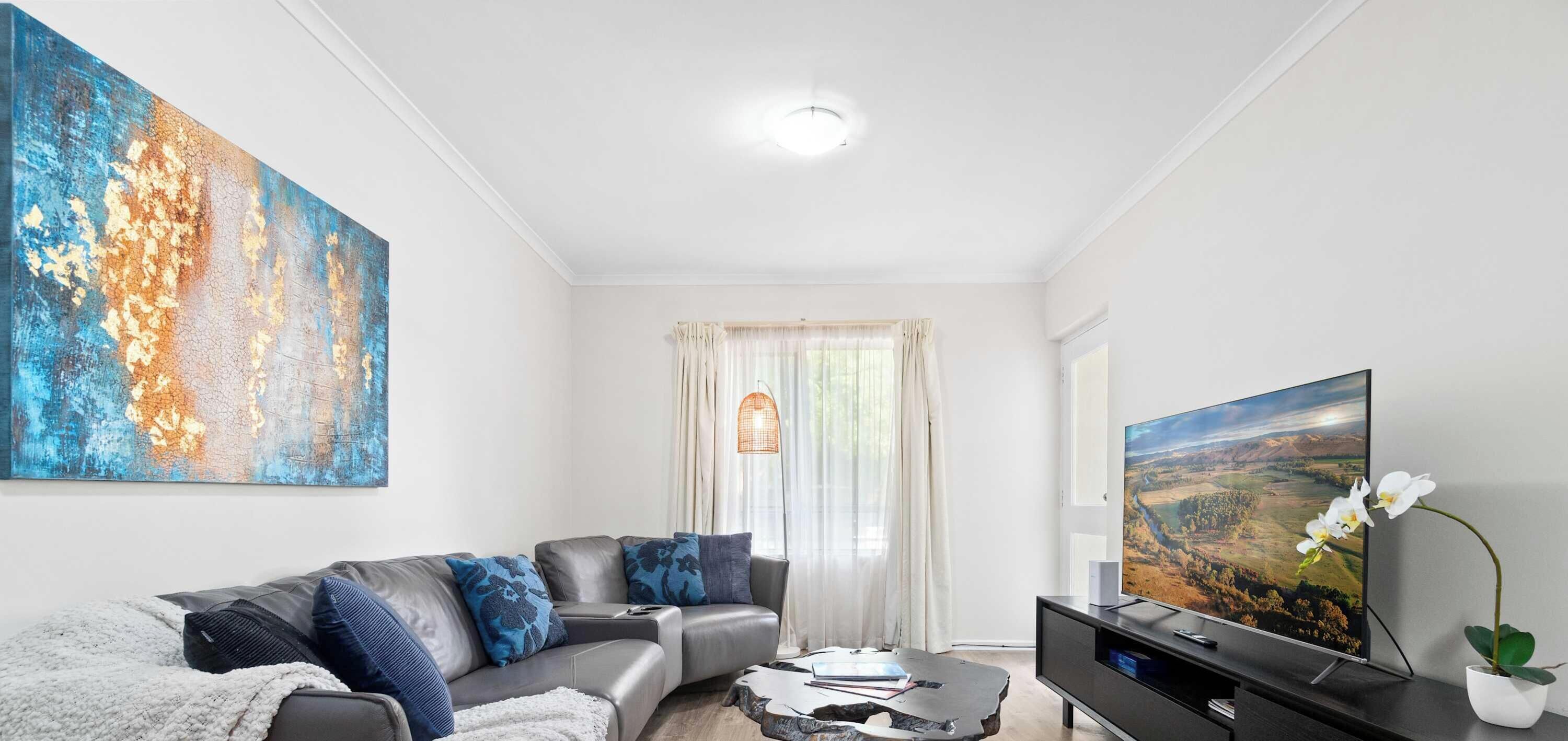 A modern living room with a sofa, a flat-screen TV, a large abstract painting, and a potted orchid.