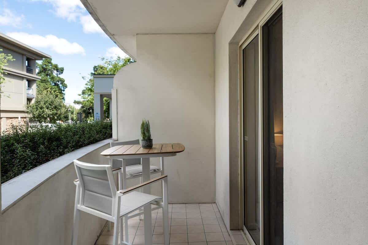 A small balcony with a table and two chairs, a potted plant, and a sliding glass door.