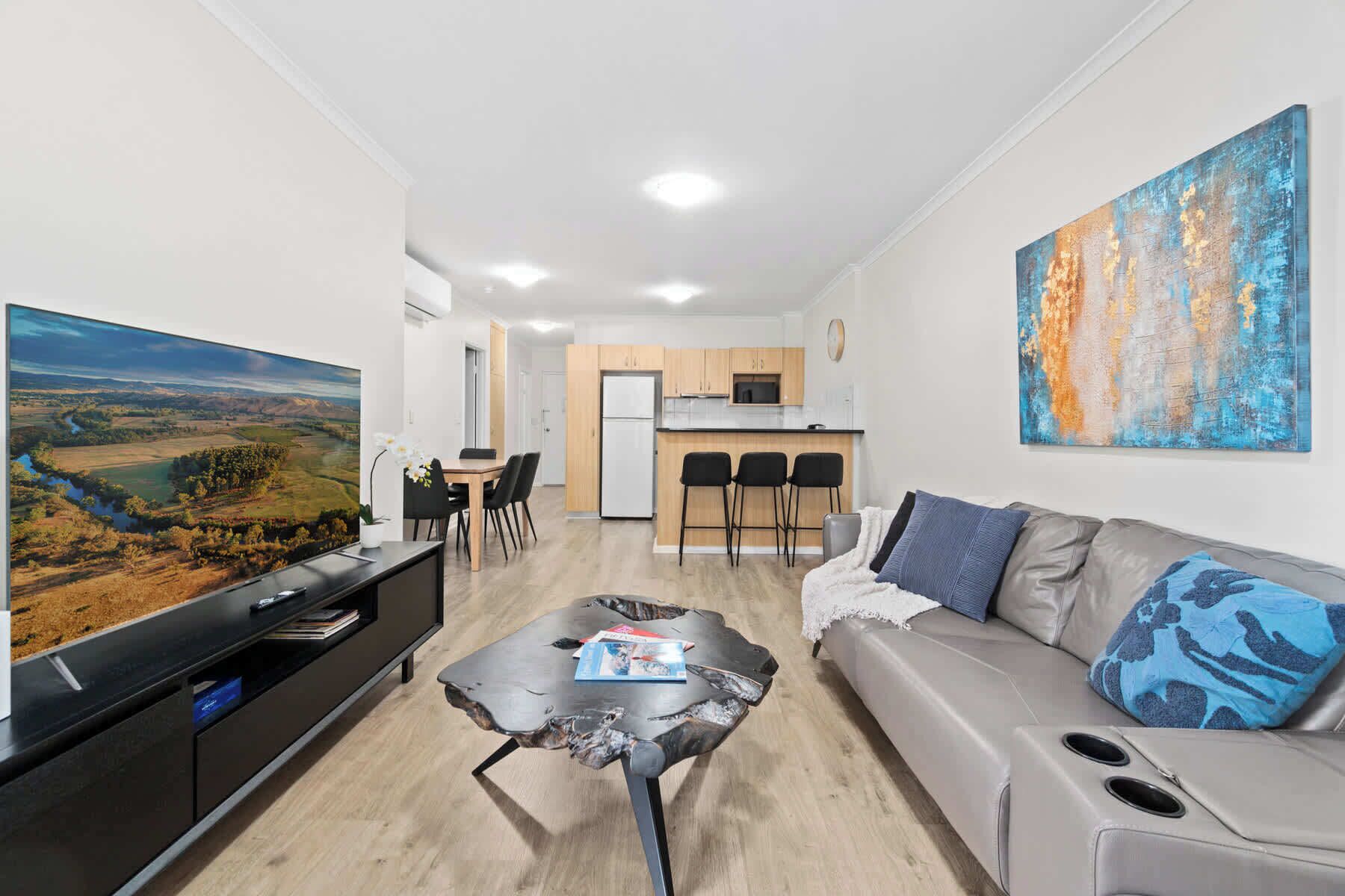 A modern living room with a flat-screen TV, a coffee table, a sofa, and a painting on the wall.