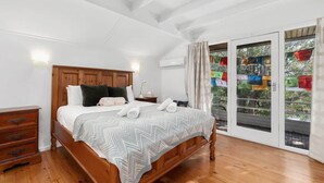 Une chambre à coucher avec un lit en bois, une table de chevet, une commode et une grande fenêtre avec des rideaux.