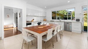 Une cuisine moderne avec des meubles blancs, une table à manger en bois et une grande fenêtre donnant sur l’extérieur.