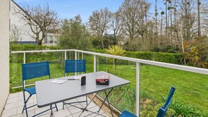 Een terras met tafel en stoelen, omringd door een hekwerk en groen.