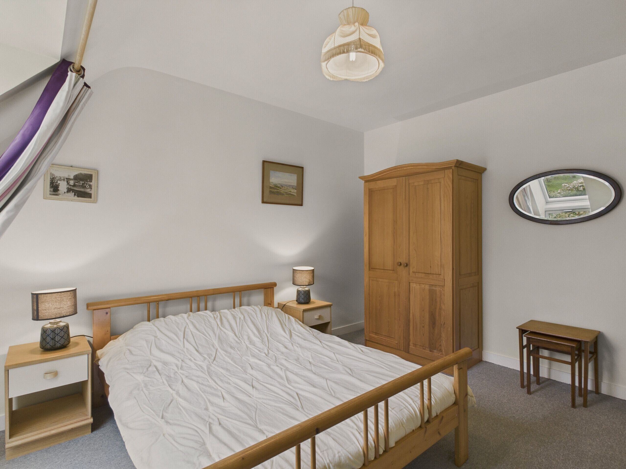 A bedroom with a wooden bed, bedside tables, a nightstand, a wardrobe, a mirror, and a hanging light fixture.