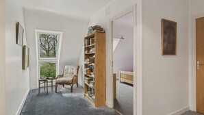 Een kamer met een groot raam, een boekenkast, een stoel en een bed.
